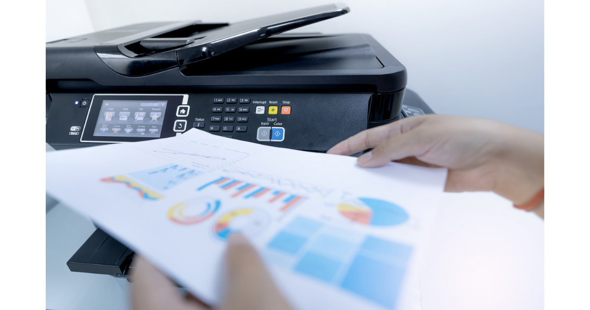 Hands holding a printed chart with colorful graphs in front of a modern multifunction printer, showcasing efficient document printing and management.